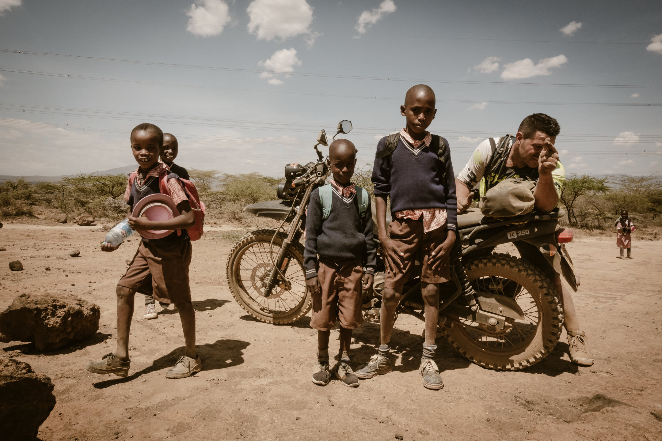 Un grupo de niños escolares se encuentra con un motociclista de RAFIKI en un paisaje árido de Kenya
