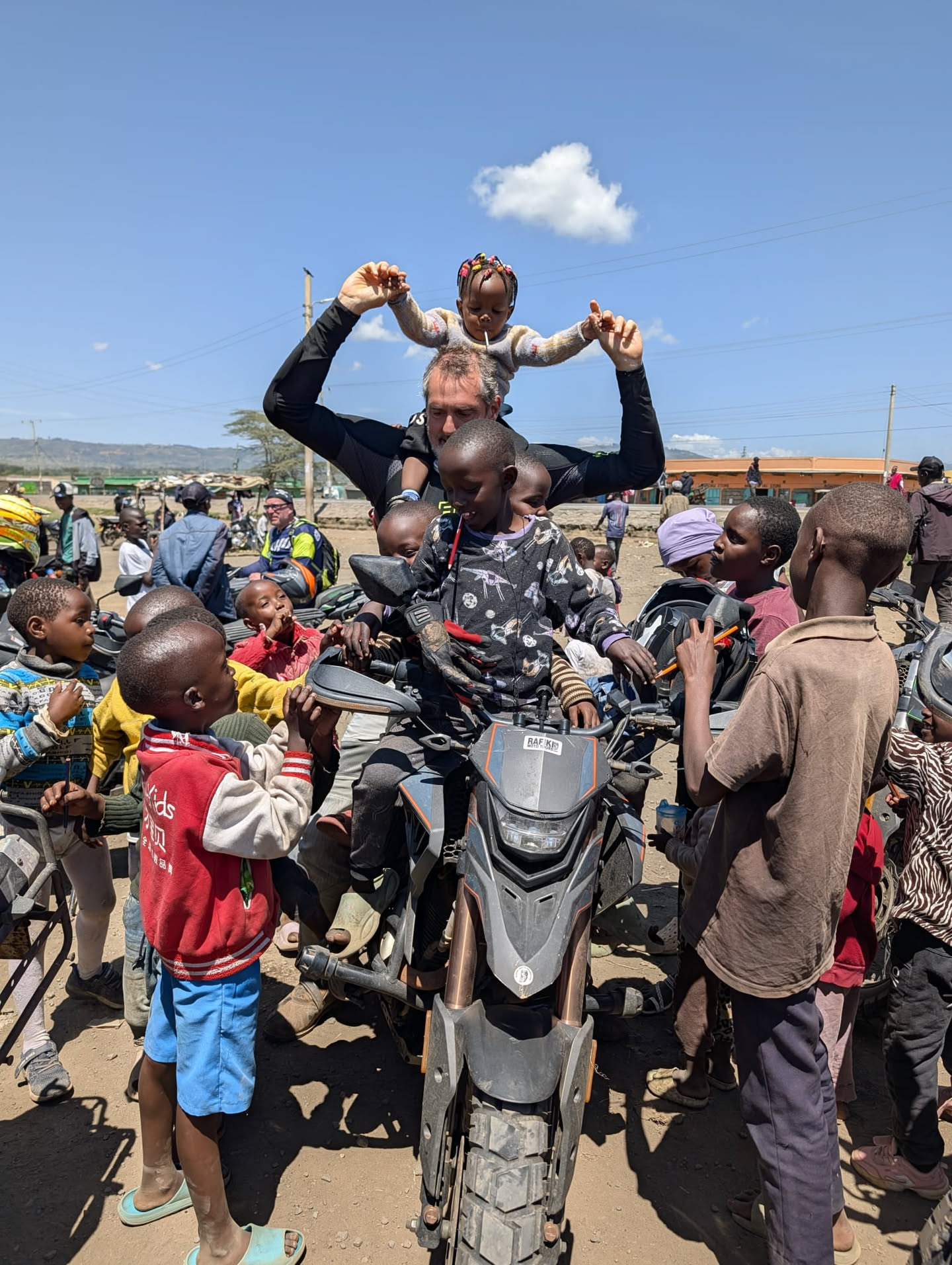 Un niño a hombros del guía de RAFIKI, rodeado de otros niños entusiastas en Kenya